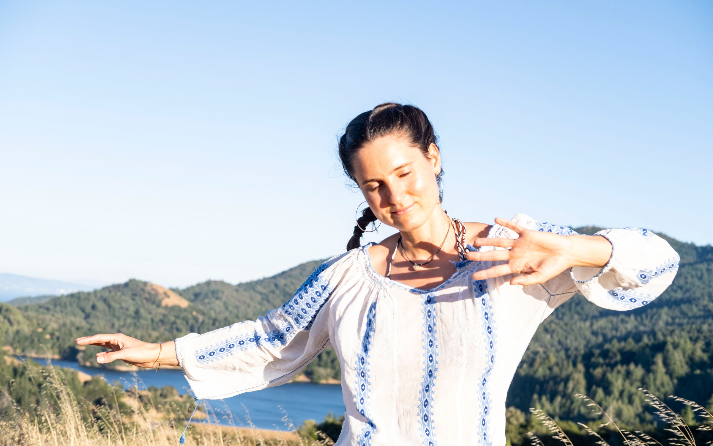 Coco Borsche in gentle movement with arms extended, hills and a lake behind her in Marin County, California